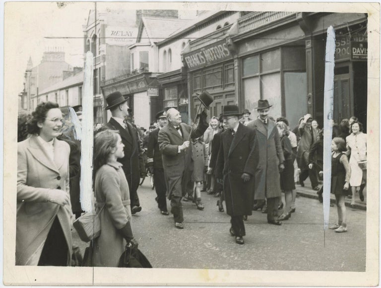 Item #005206 An original wartime press photograph of Prime Minister Winston S. Churchill followed by cheering crowds as he surveys bomb damage on 12 April 1941, during the last weeks of The Blitz