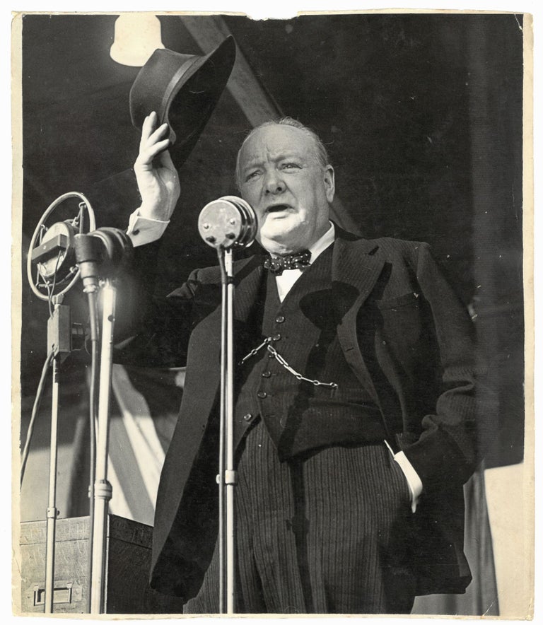 Item #005357 An original wartime press photograph of Prime Minister Winston S. Churchill on 3 July 1945, keeping the sun out of his eyes with a borrowed hat while delivering his final campaign speech for the General Election that ended his wartime premiership